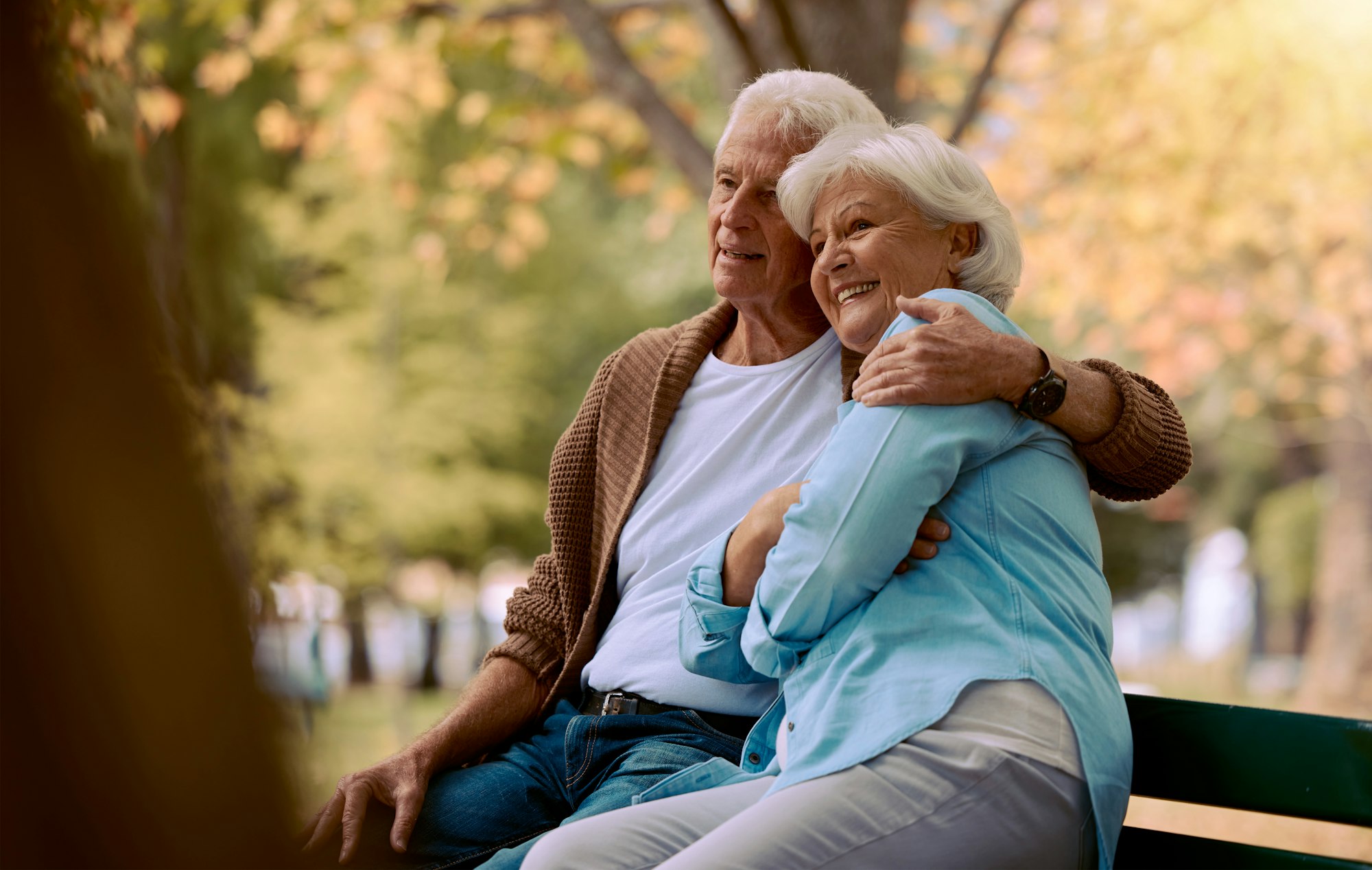 Couple, elderly and hug in park during retirement, sitting on park bench with love and spending qua