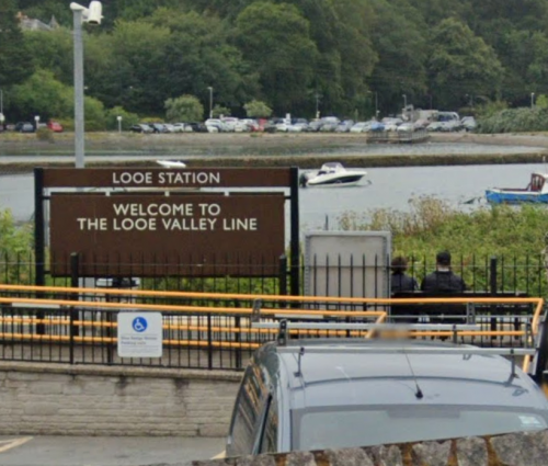 Looe railway Sign at Looe Station welcoming visitors to the Looe Valley Line, with boats in the background.